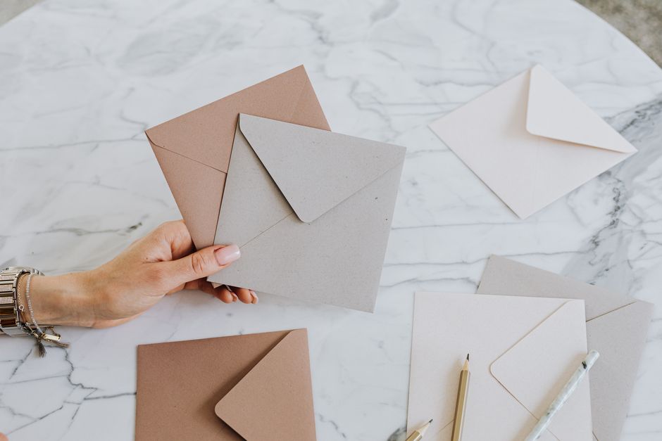 A hand holding craft envelopes on a stylish marble table with pencils, showcasing an artistic layout.