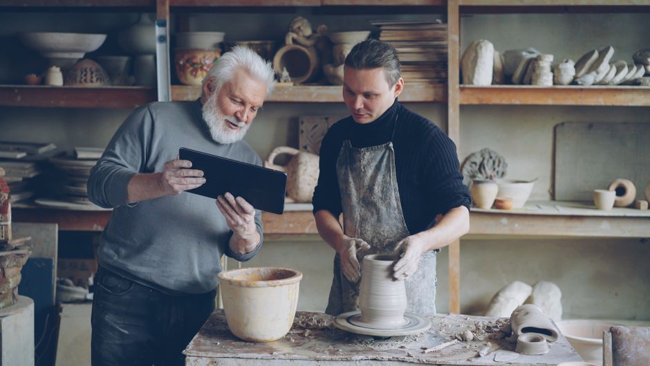 Elderly instructor guiding young student in pottery class, hands-on learning session.