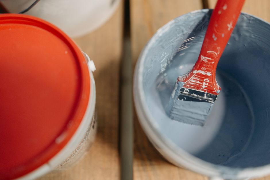 Red brush dipped in blue paint bucket, ready for painting projects.